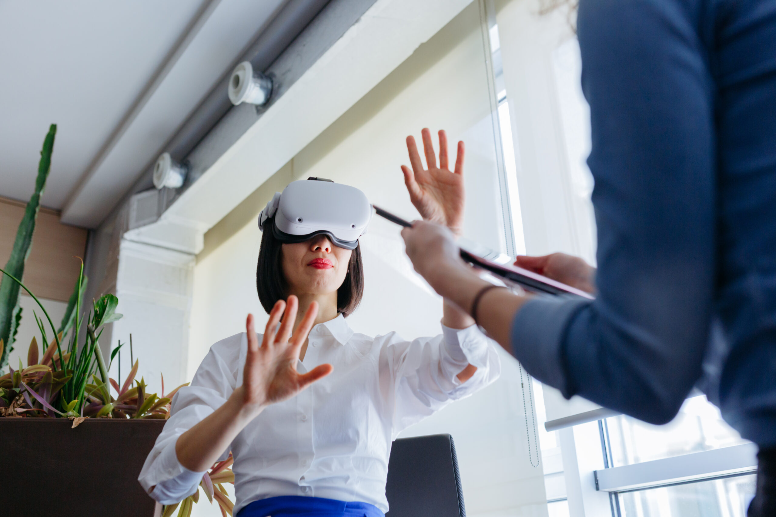 sitting asian woman wearing viewer exploring virtual reality with her colleague